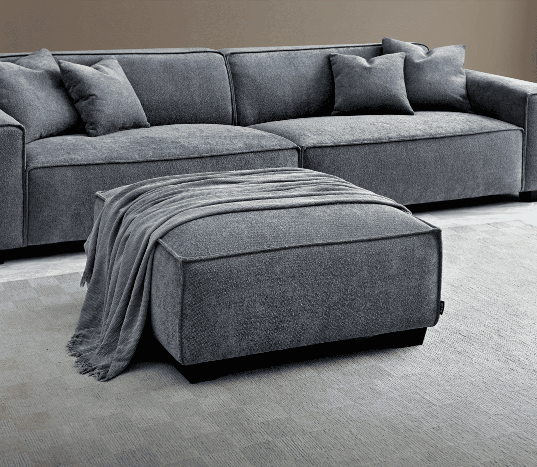 The Aluxo Dakota Sofa Range in Charcoal Boucle, elegantly styled with a footstool and soft blanket in a modern living space.